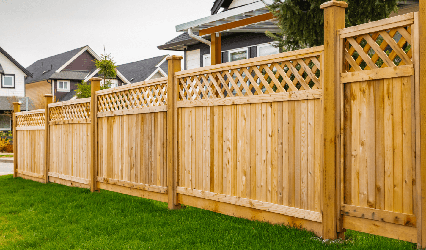 Wooden fence with lattice top sections, dividing suburban houses and gardens, bordered by green grass.